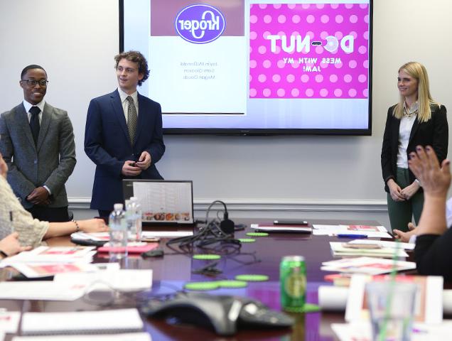 A group of students wearing business professional attire pitching an idea, 投影在他们身后的屏幕上, 敬满屋子的专业人士 