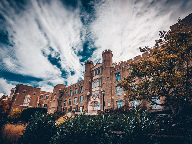 The exterior of Hinkle Hall. 欣克尔大厅是一座三层建筑，设计为都铎哥特式风格. 天空是湛蓝的，飘着缕缕云. 