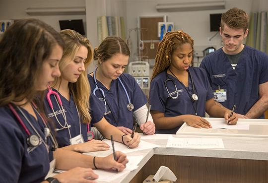 五名穿着藏青色工作服的泽维尔护理专业学生在临床环境下在纸上写字